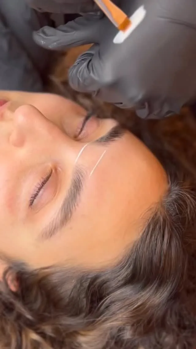 Gloved hand drawing a mapping thread across a client's brow — brow tattoo preparation