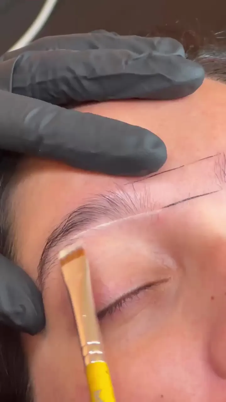 Artist laying a mapping thread across a client's eye — nano brow preparation