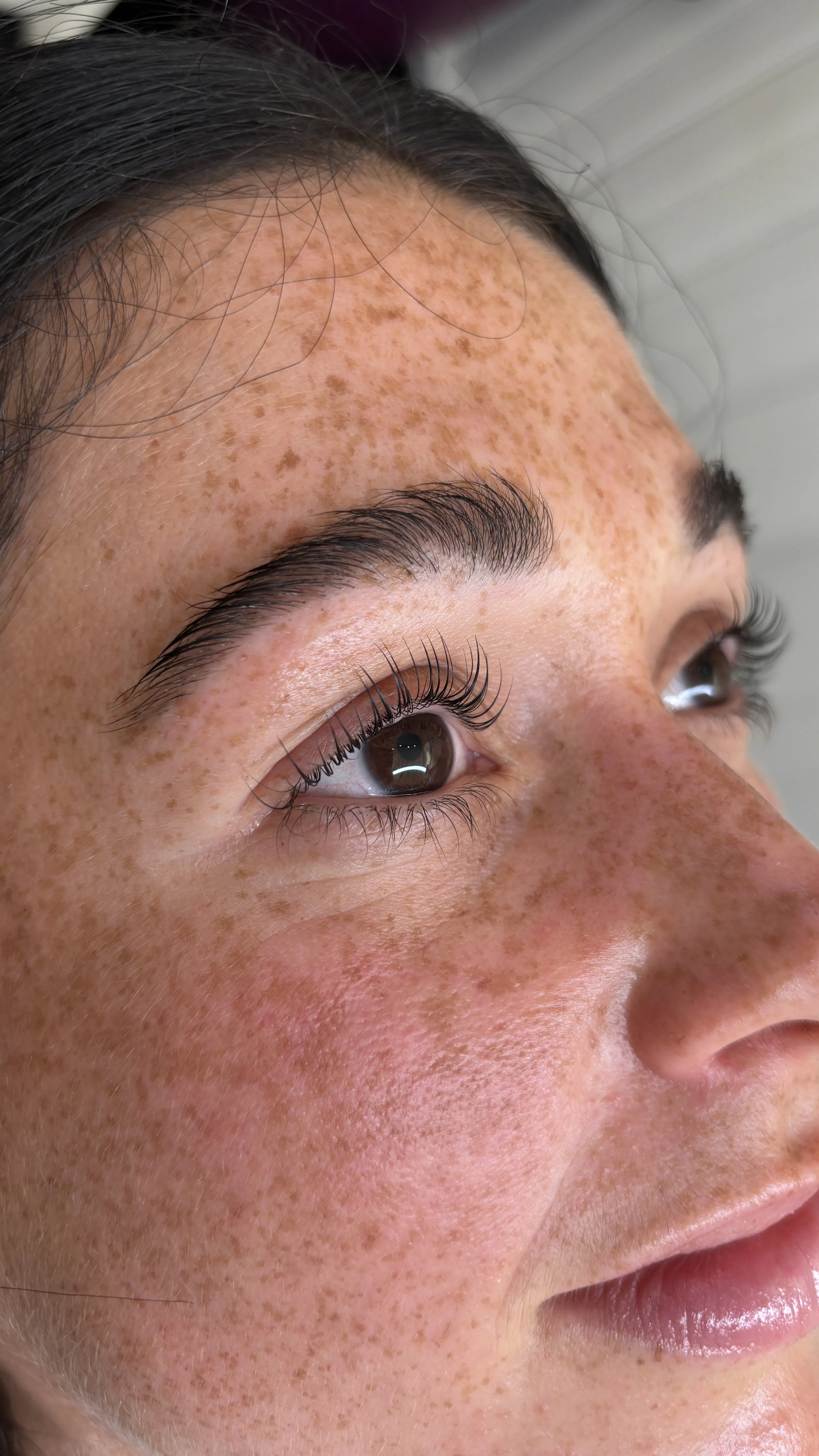 Three-quarter face of a heavily freckled client with laminated brow and lifted lashes