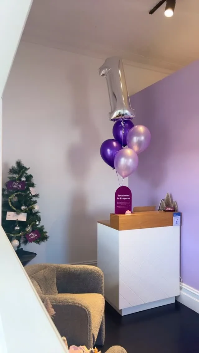 Studio reception corner at Ink & Arch Brow Bar — white desk, purple wall and arch-shaped Treatment In Progress sign