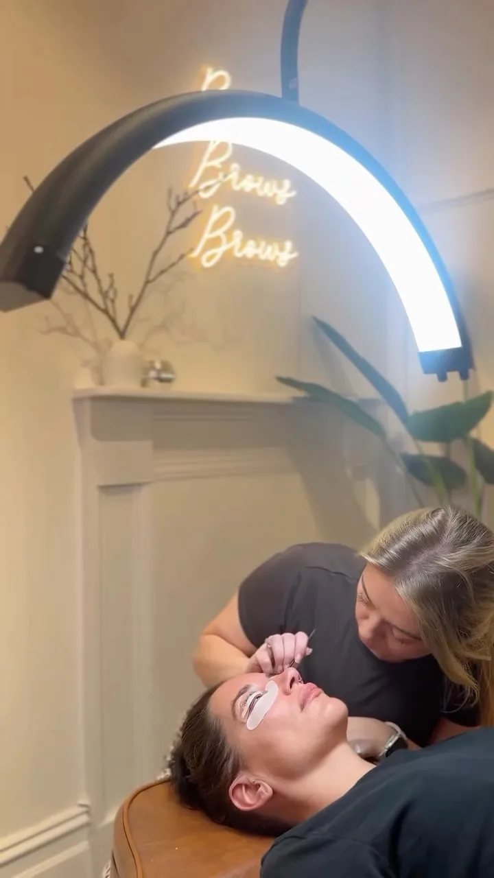 The studio's neon Brows sign above the white fireplace mantel, artist at work below
